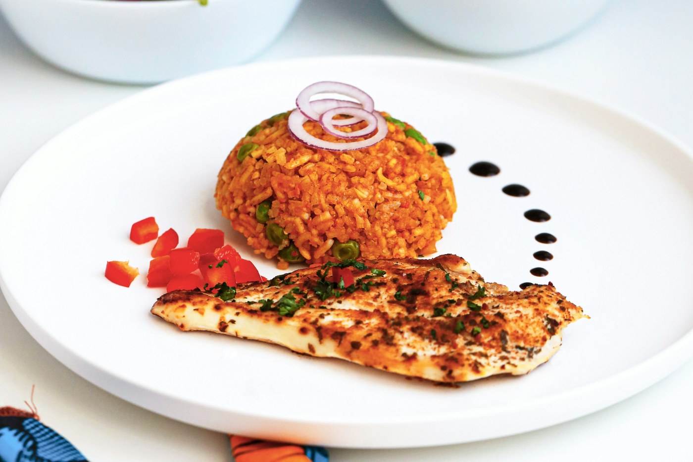 A plated serving of red-orange jollof rice with chicken and herbs.