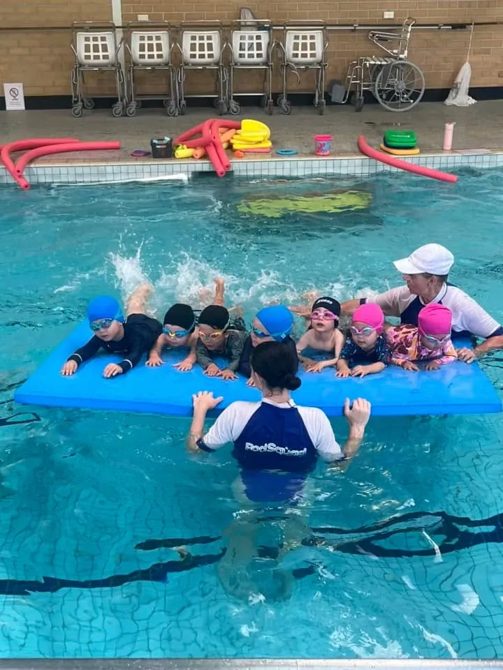 A small group of Pod Squad children kicking along a floating mat with two instructors
