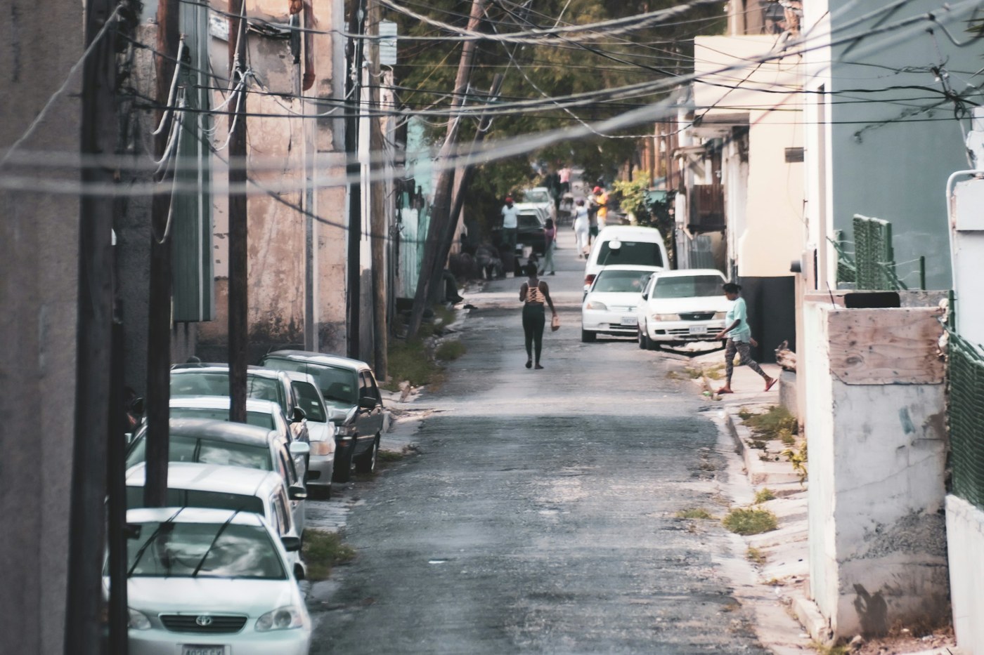 Parked cars and low-rise buildings along a sunlit urban street in Kingston, Jamaica.