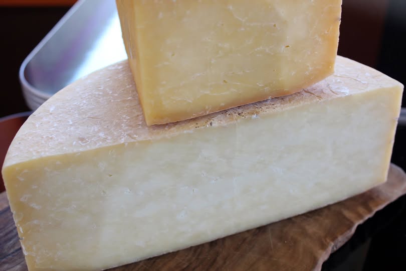 a quarter of a dense and hard looking cheese on a half cycle of cheese and the cheese being great lakes cheshire
