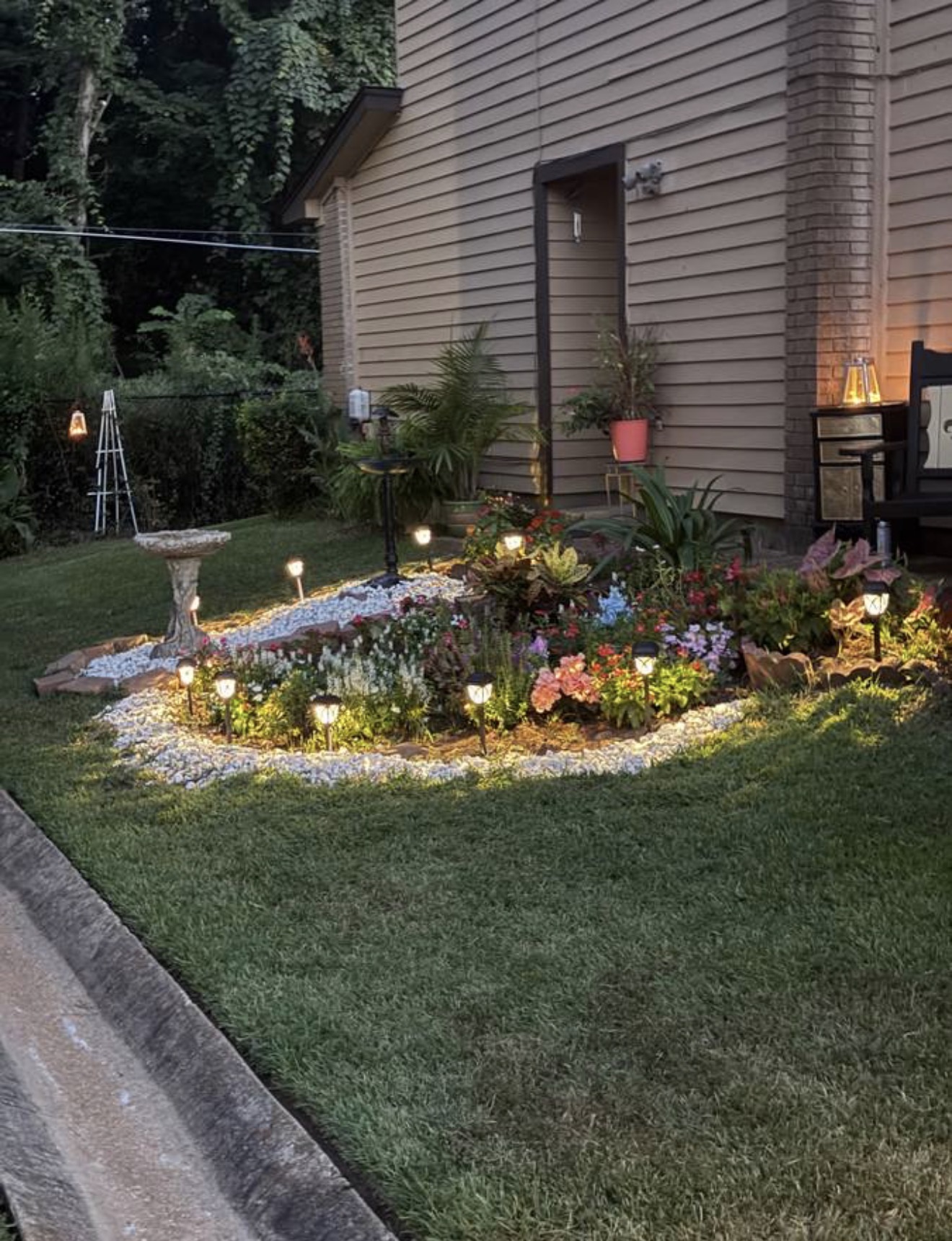 Front garden bed at dusk with path lights glowing along a white stone border