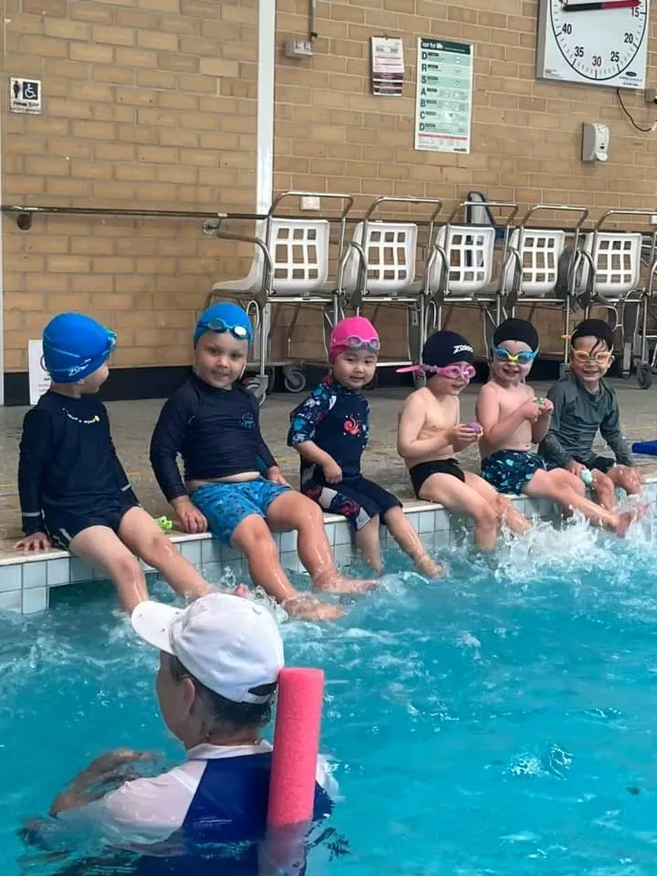 Young Pod Squad swimmers sitting along the pool edge ready for their lesson