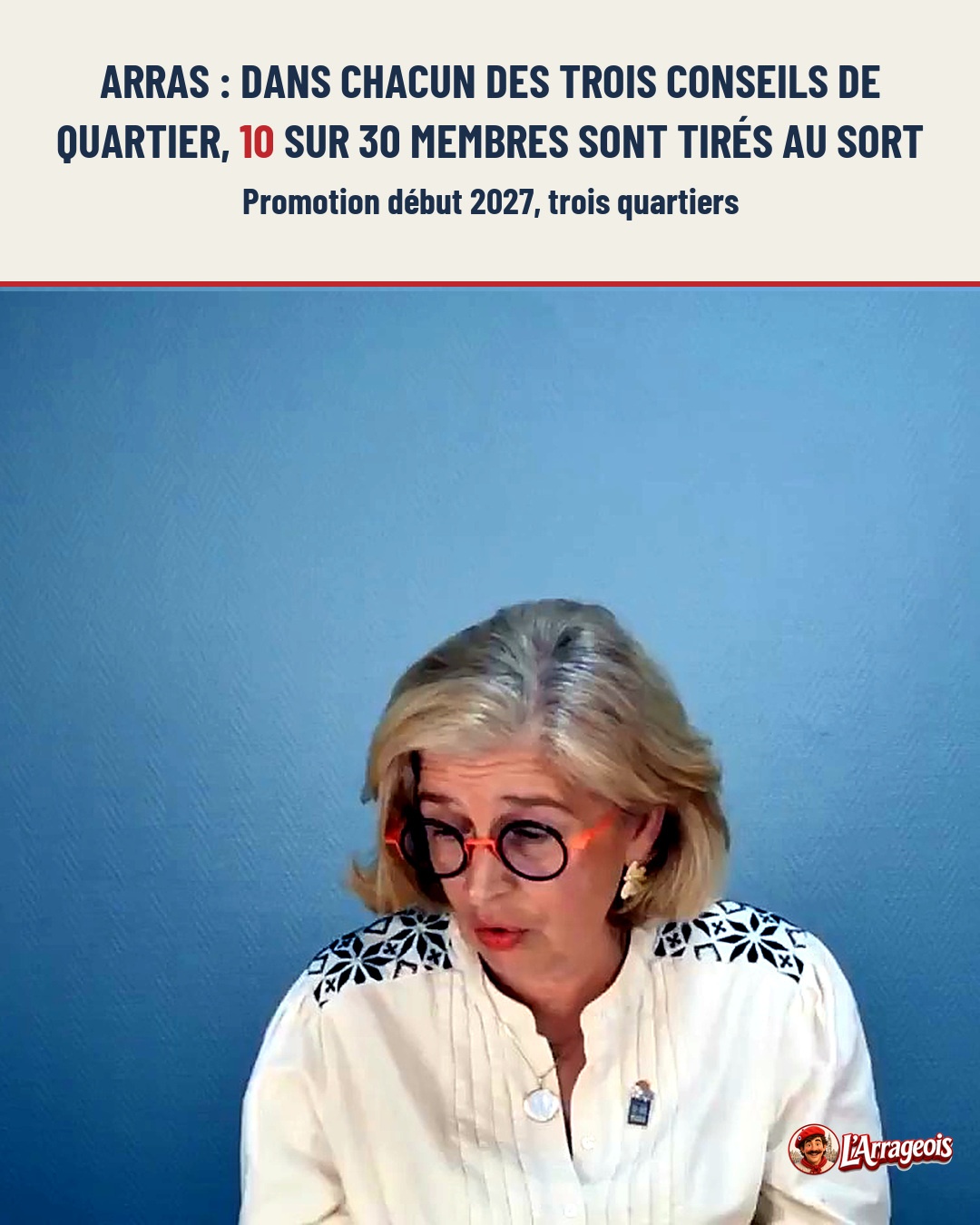 Une femme blonde aux lunettes orange, portant une blouse blanche brodée, parle devant un fond bleu uni.
