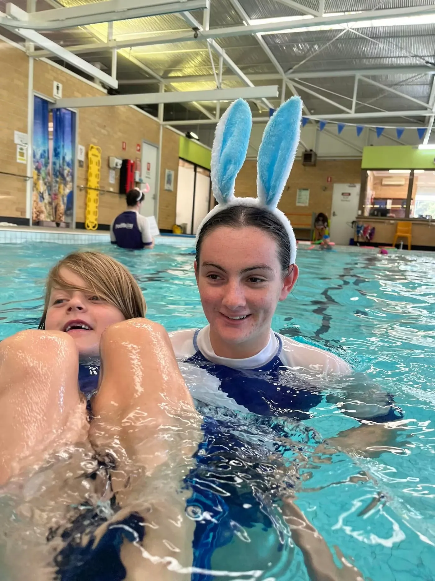 A Pod Squad instructor supporting a smiling child in the pool