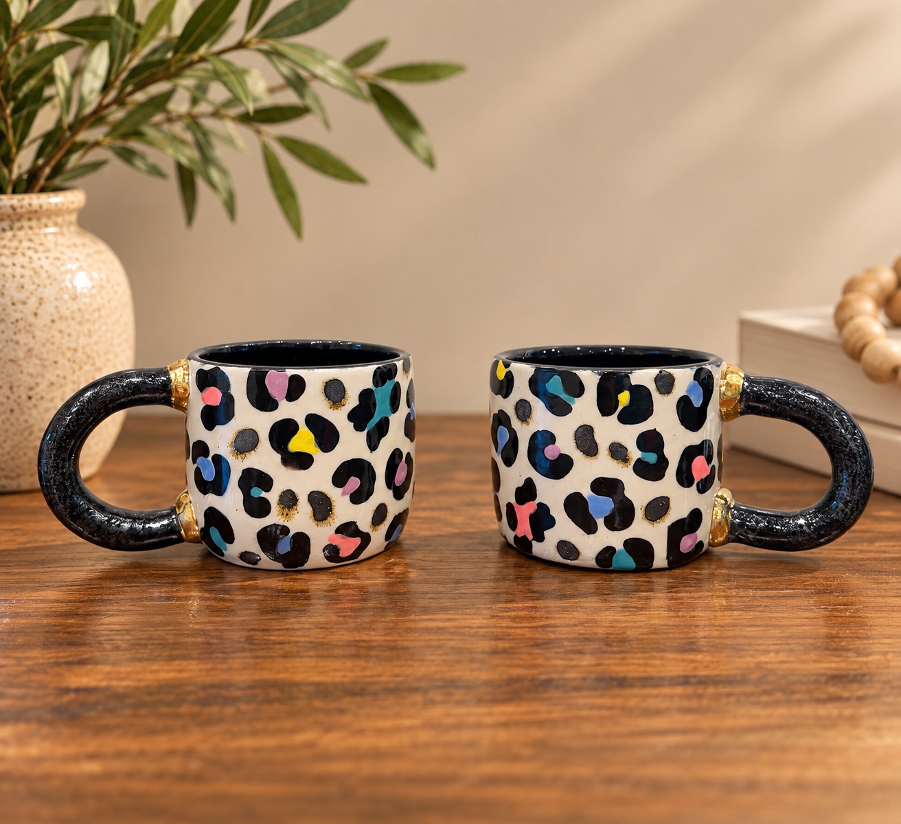 Two hand-built cups in white with black and multicolor leopard print and gold luster handles