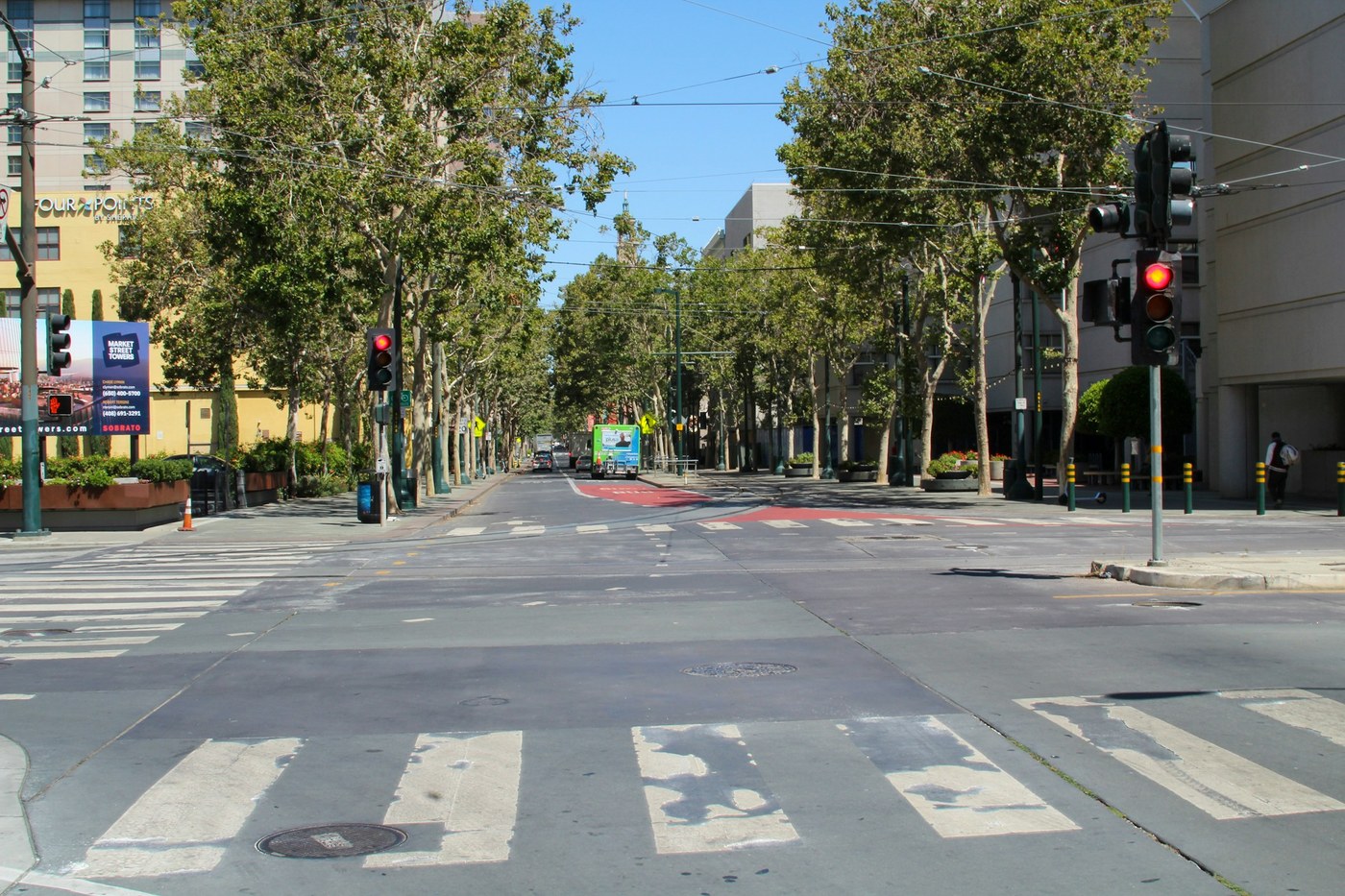 Pedestrians cross a broad downtown San Jose intersection between mid-rise buildings and traffic lights.