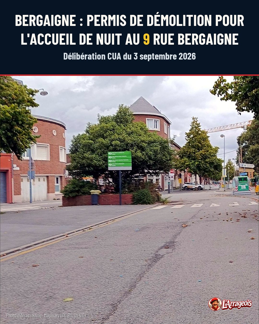 Rue pavée avec immeubles en brique, arbres, panneau vert et voiture au loin sous un ciel nuageux.