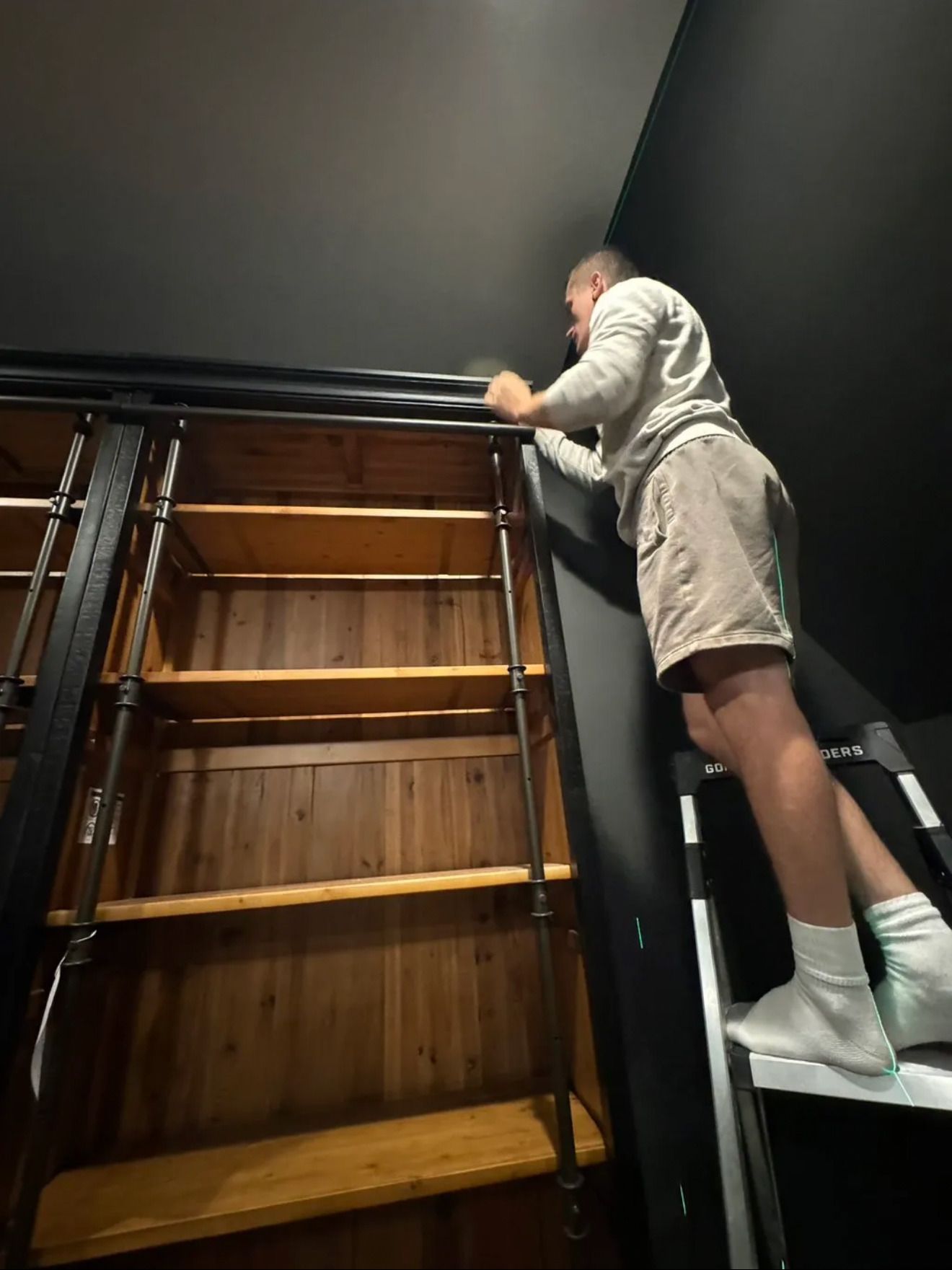 Aleh on a ladder, adjusting the top of a tall wooden bookcase