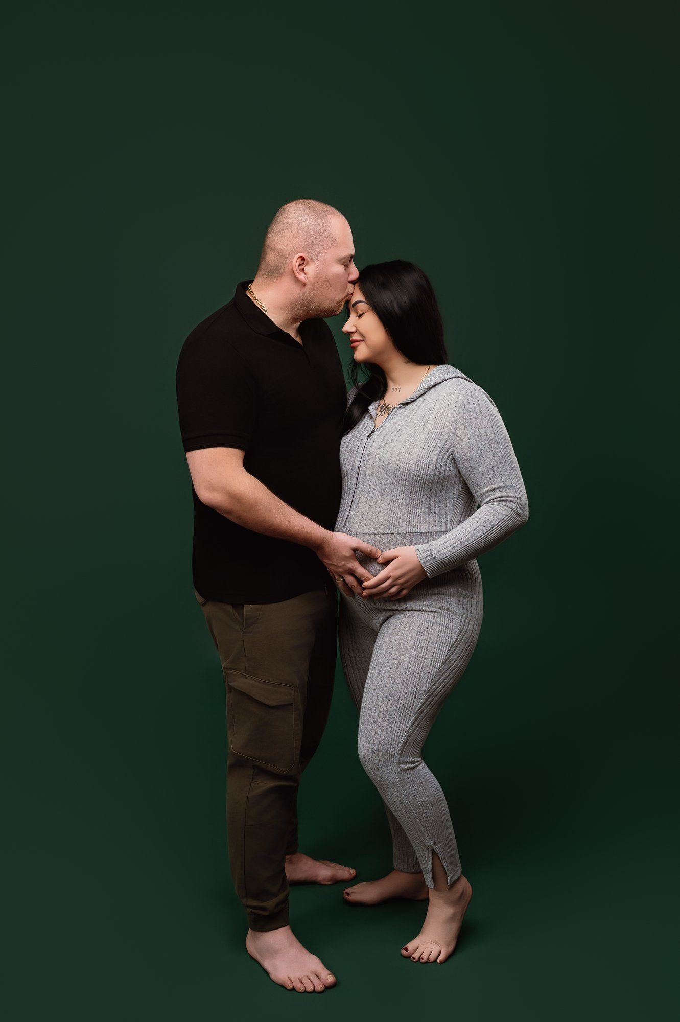 Pregnant woman in grey ribbed dress with partner's hand on her bump, intimate maternity pose