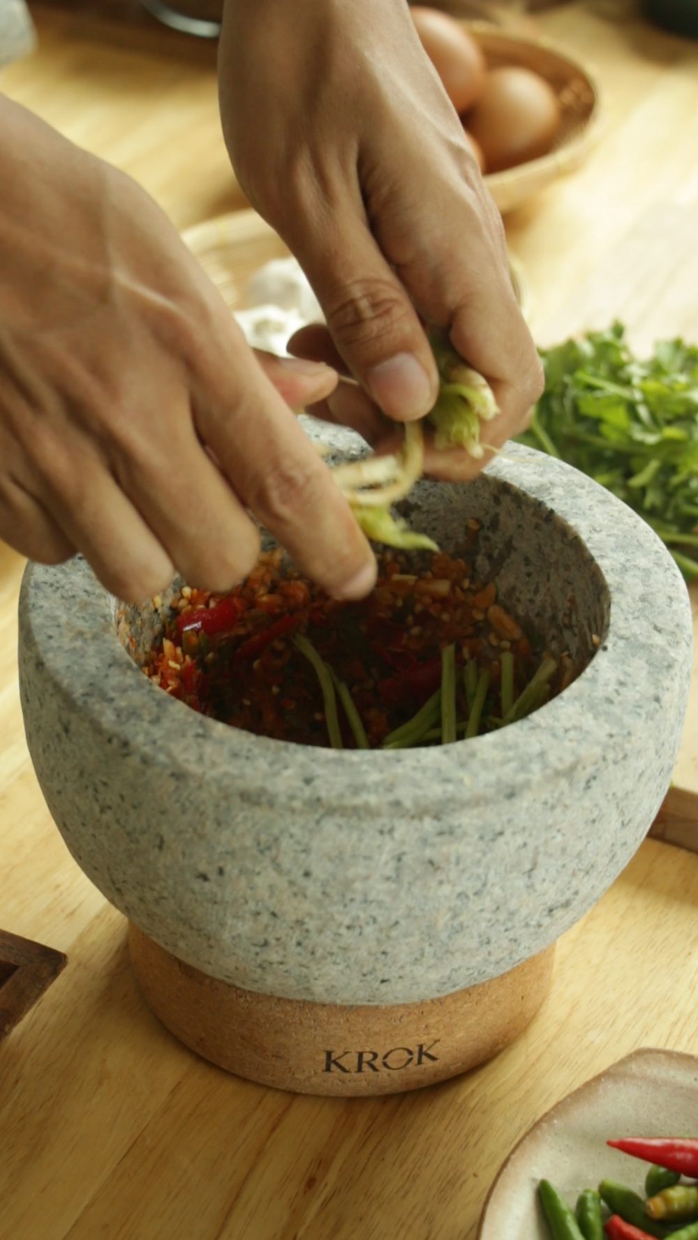 Adding coriander roots to pounded chili and garlic paste in KROK mortar
