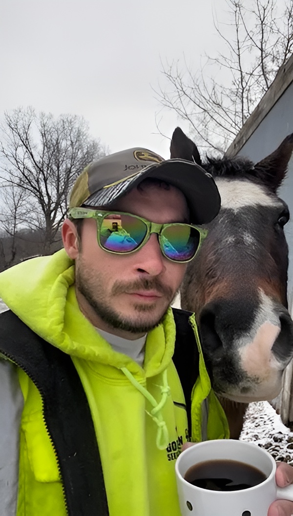 A photo of Jordan Wagoner posing near a horse with a cup of coffee in his hand