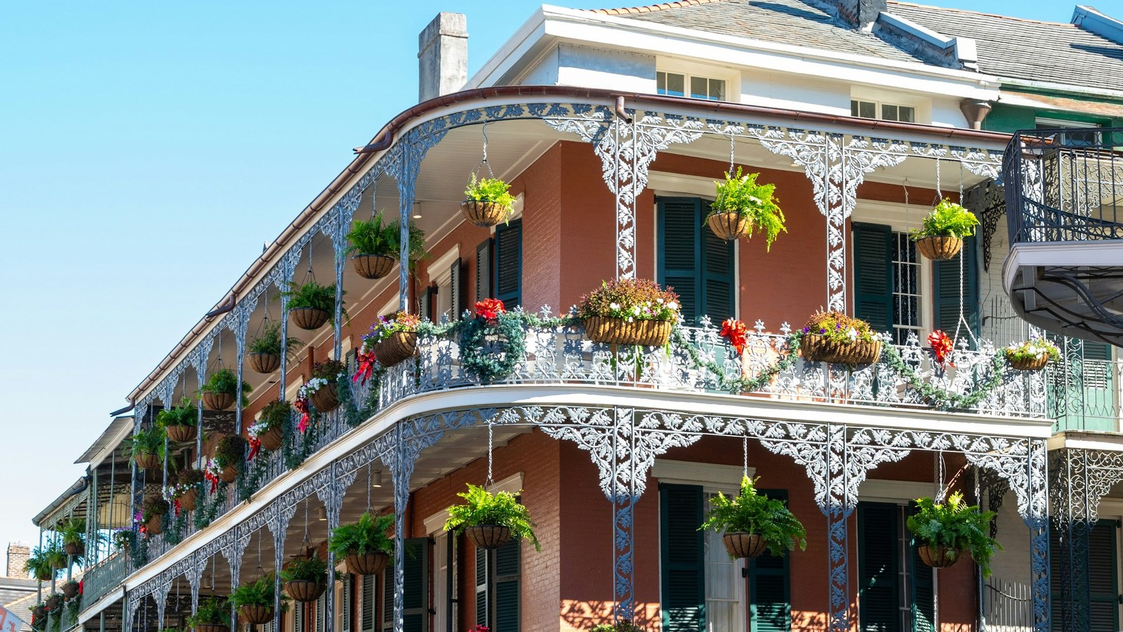 A New Orleans facade with ornate iron balconies, flowering plants and tall shuttered windows.
