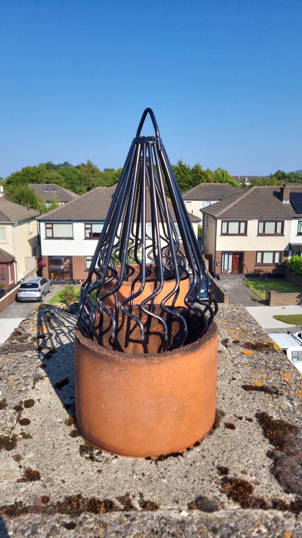Anti-bird cowl fitted to a chimney pot, rooftop view against blue sky