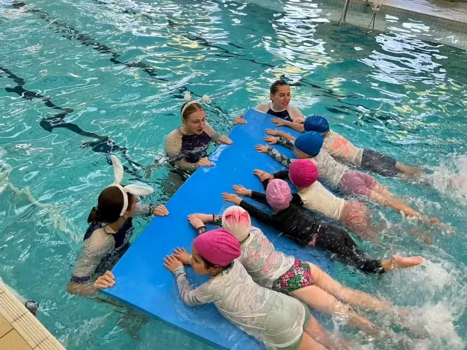 A small group of school-aged Pod Squad swimmers kicking along a floating mat
