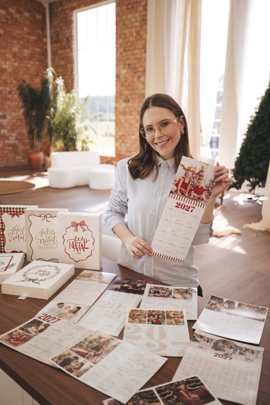 Tarcy no estúdio com os calendários 2027 e as caixas de Natal sobre a mesa