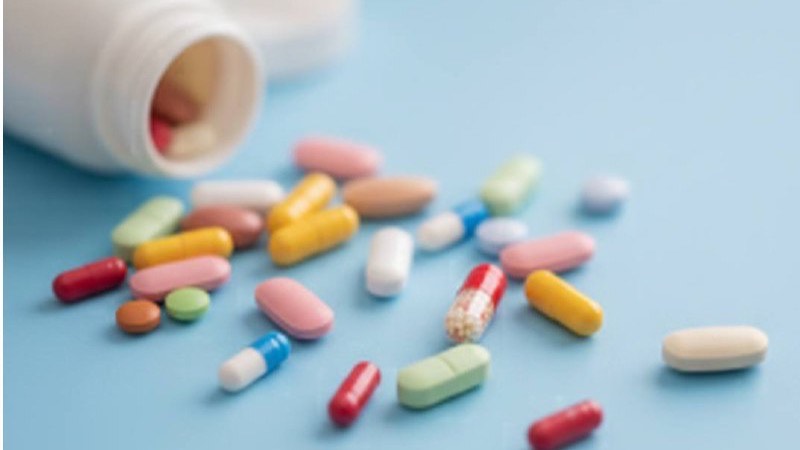 Colorful prescription pills and capsules spilling from a white medication bottle on a blue background
