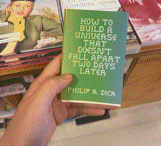 me holing a tiny book called 'HOW TO BUILD A UNIVERSE THAT DOESNT FALL APART TWO DAYS LATER' by Philip K. Dick
