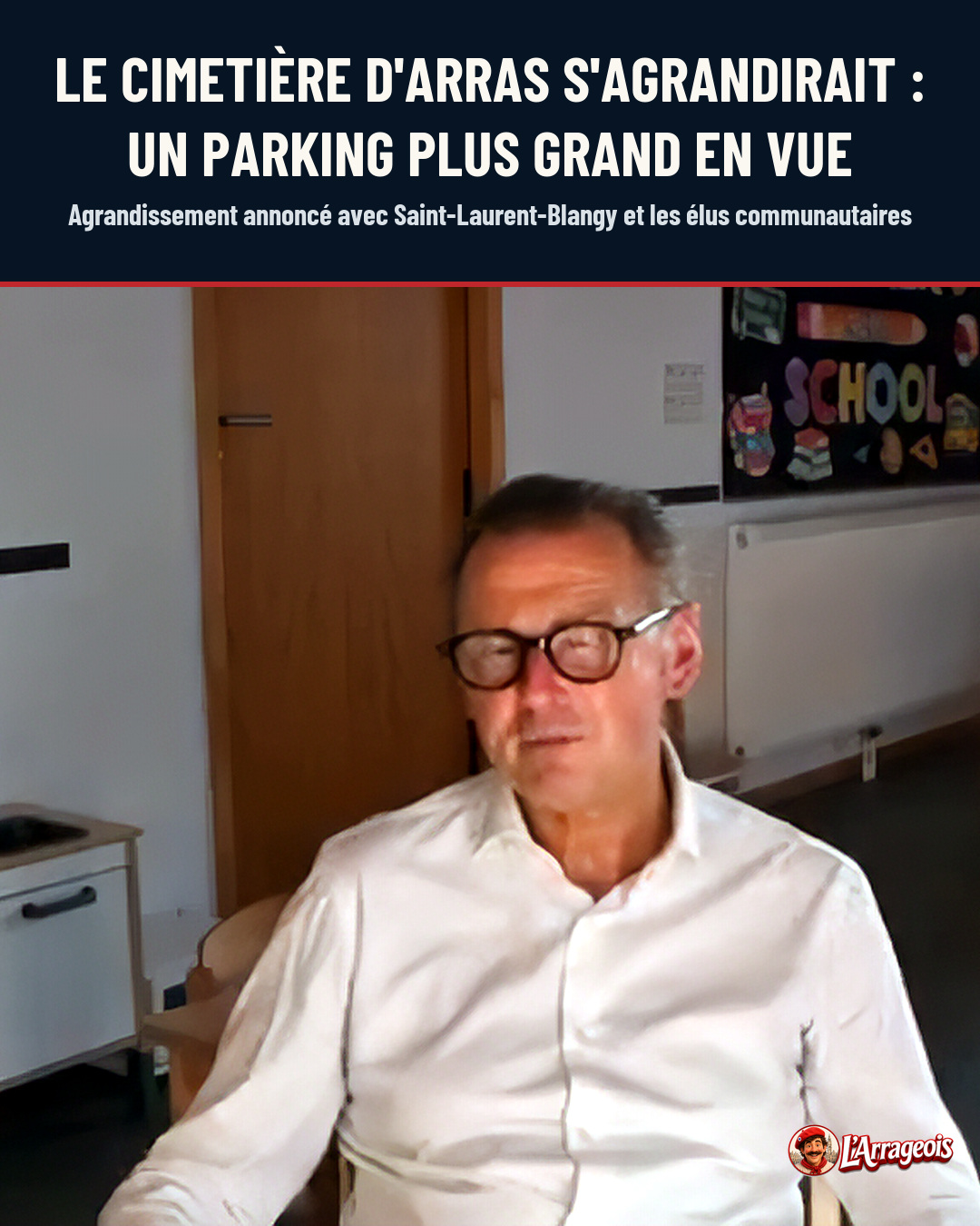 Un homme âgé portant des lunettes et une chemise blanche est assis dans une pièce intérieure avec une porte et un tableau d'école en arrière-plan.