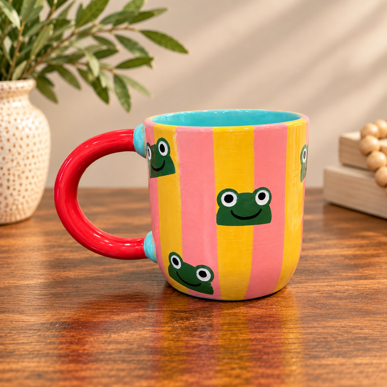 Lisa's frog mug: pink, orange and yellow vertical stripes with hand-painted green frog faces and a red handle