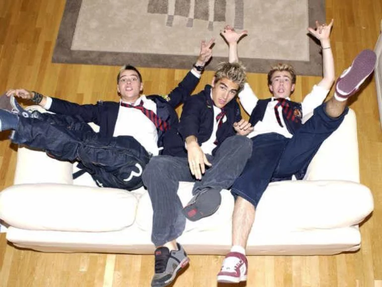 Busted lounging upside-down on a white sofa in school uniforms, shot from above