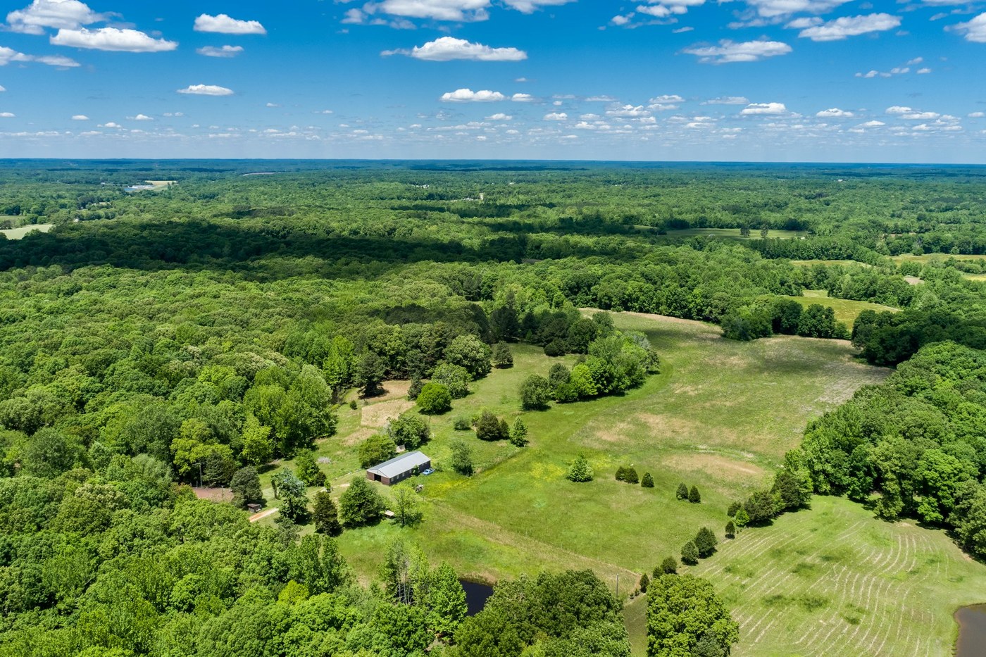 An aerial view of green Tennessee farmland stretching toward low wooded hills beneath a blue sky.