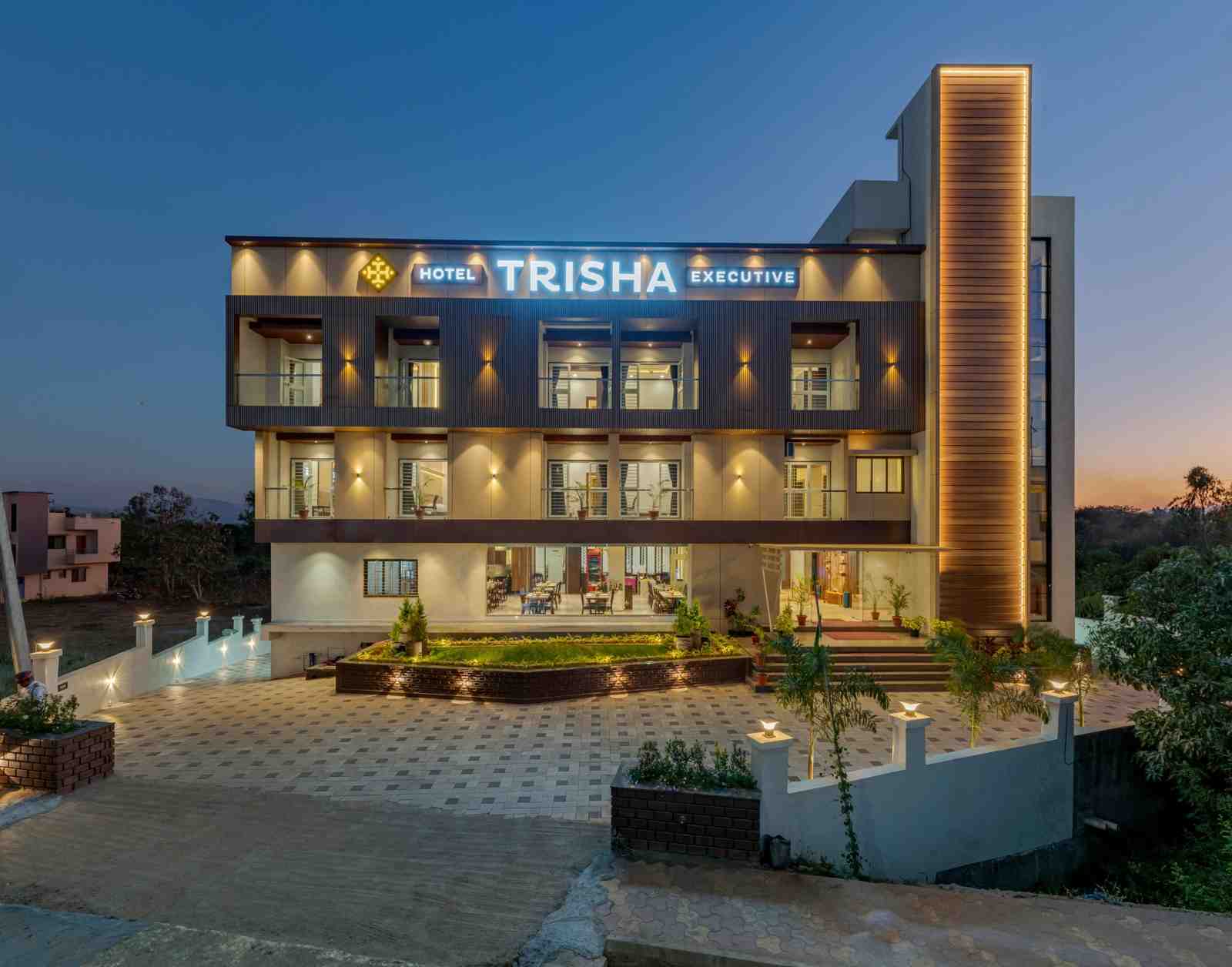 Actual exterior of Hotel Trisha Executive illuminated in the evening in Adamapur, Kolhapur