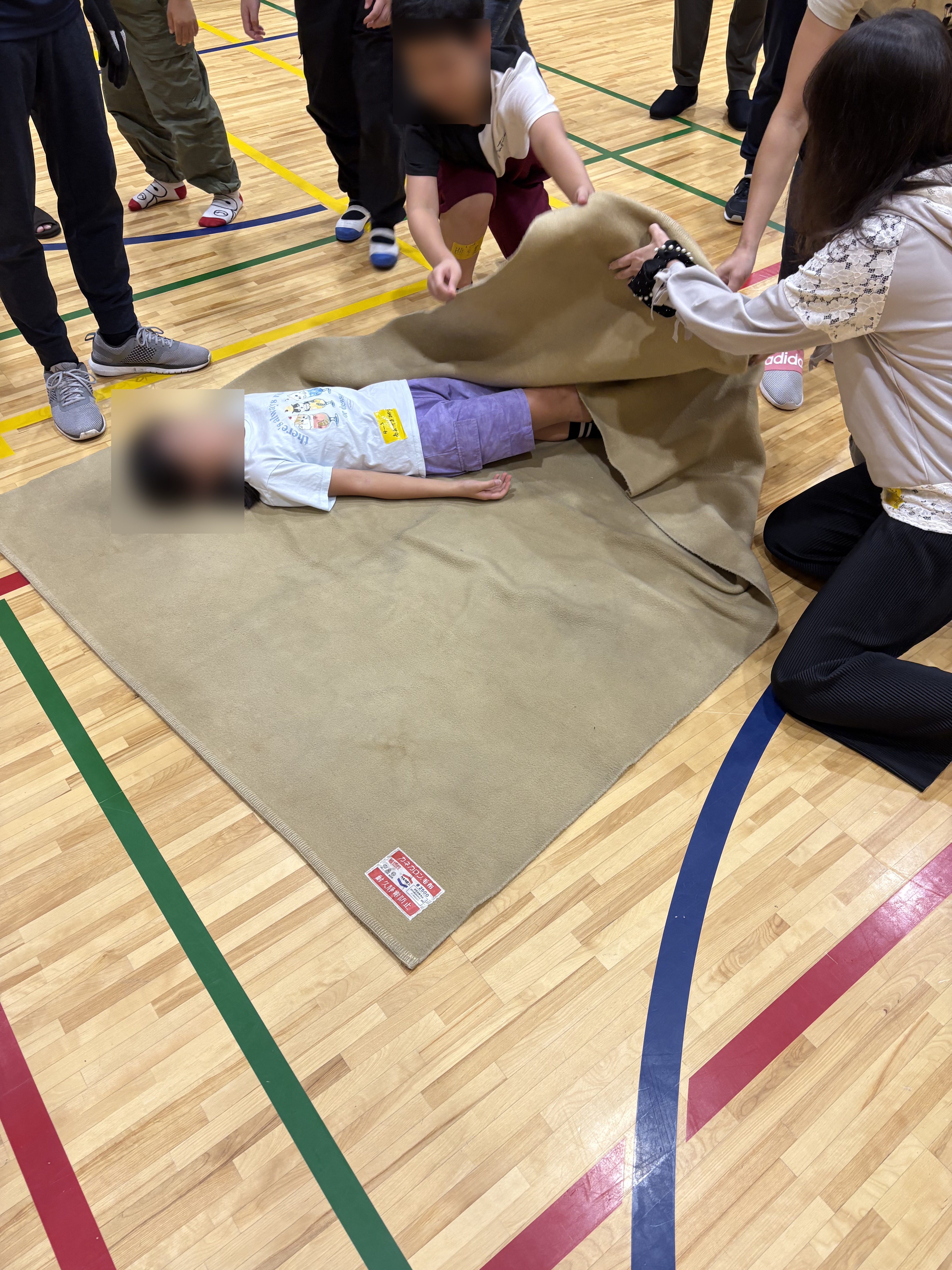 毛布に乗り担架搬送訓練を受ける子供