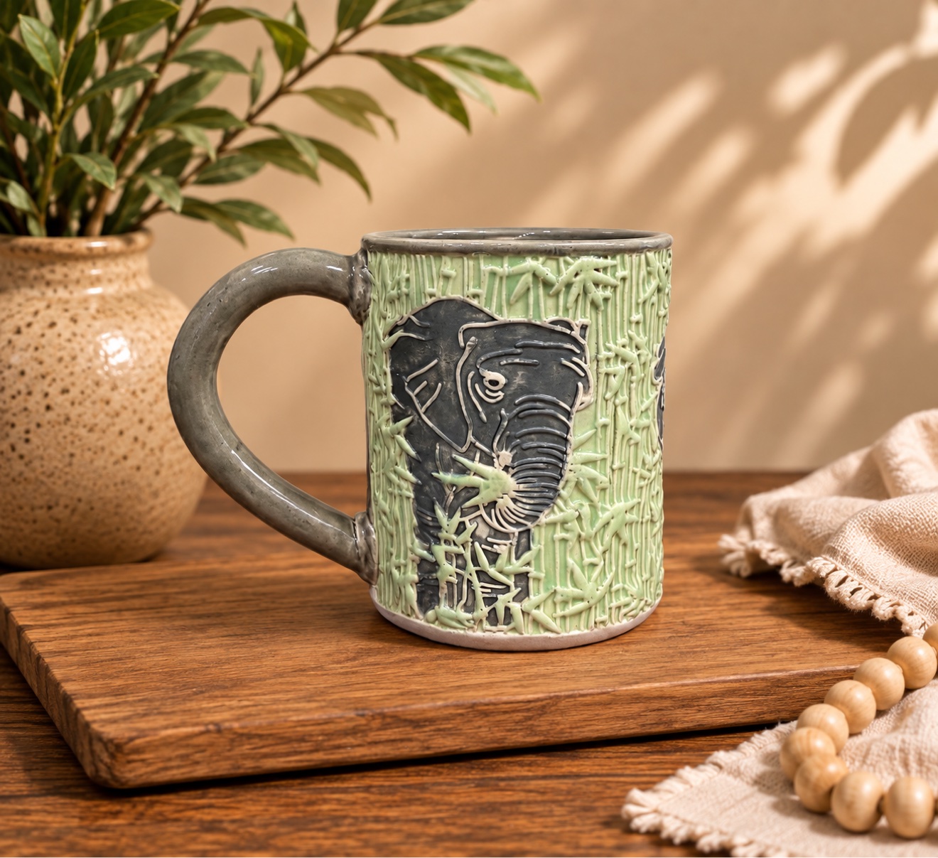 Lisa's elephant mug: light green sgraffito bamboo-textured mug with a dark gray elephant face and matching gray handle, on a wooden table
