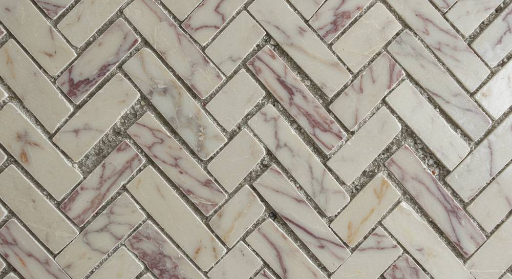 An artisan's hands creating a hand-cut modern abstract mosaic, showcasing raw stone tesserae and tactile topography in progress.