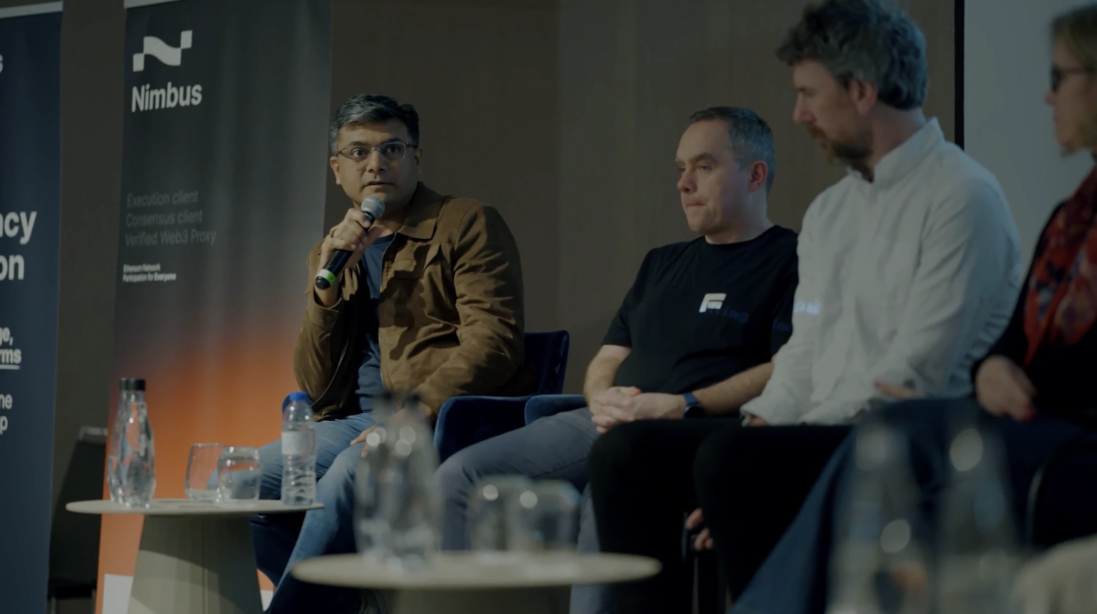 Three-man panel discussion on stage at the Parallel Society Festival with Nimbus banners behind them