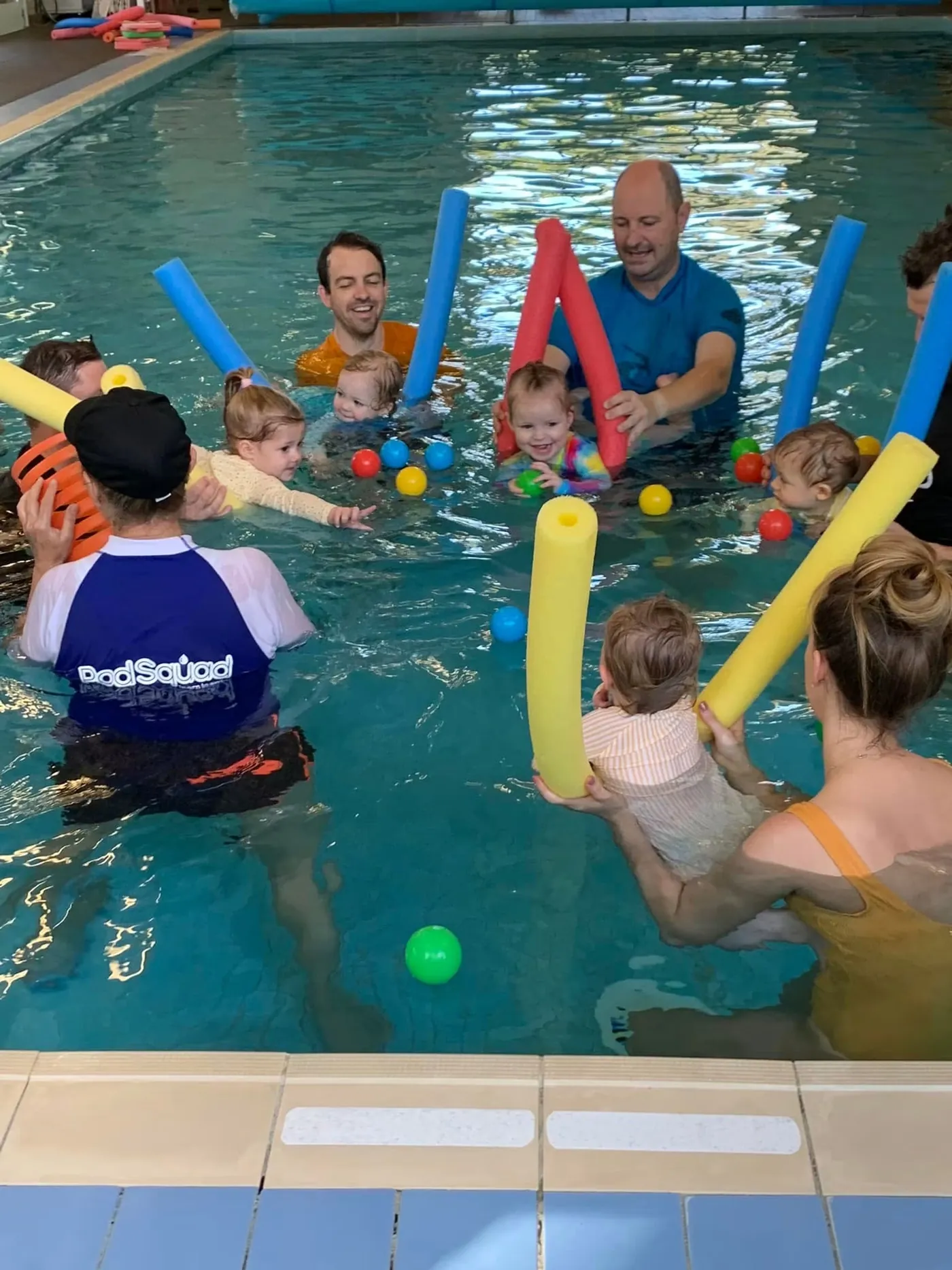 A Pod Squad parent-and-baby class playing with pool noodles in the warm indoor pool