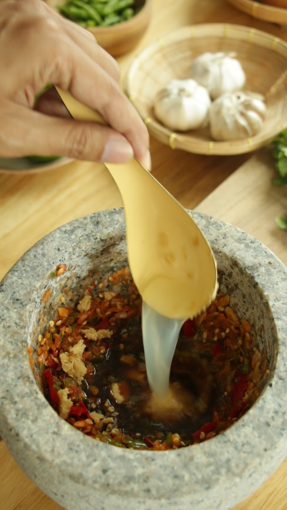 Adding lime juice and fish sauce to the pounded chili paste for Nam Jim