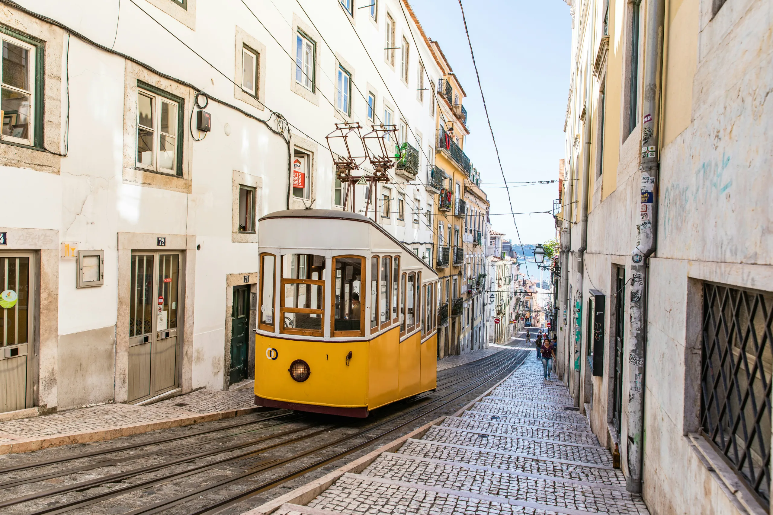 An iconic yellow Lisbon tram travelling along a cobblestone street in the old town