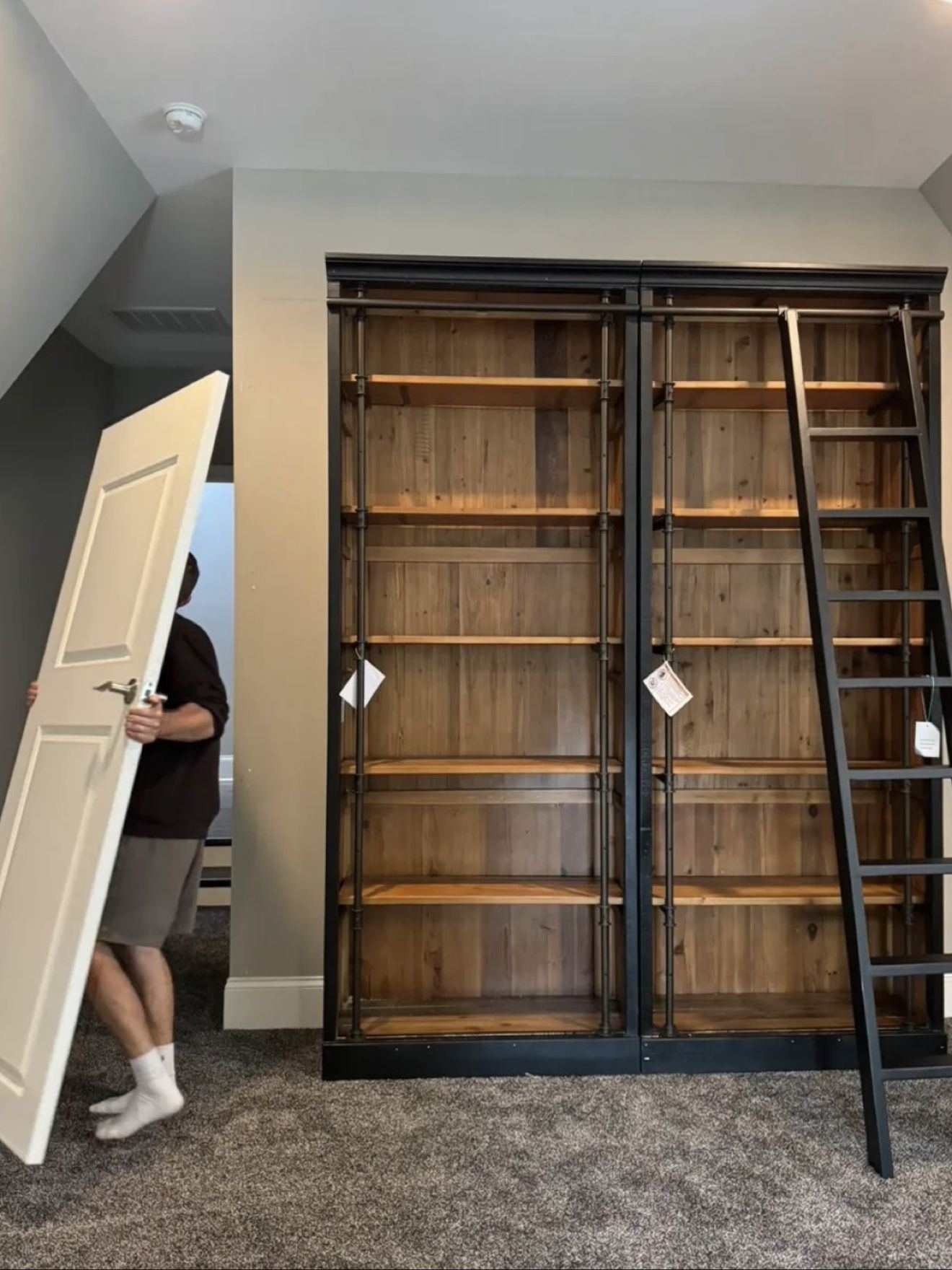 A door being carried in beside a tall wooden bookcase with a ladder