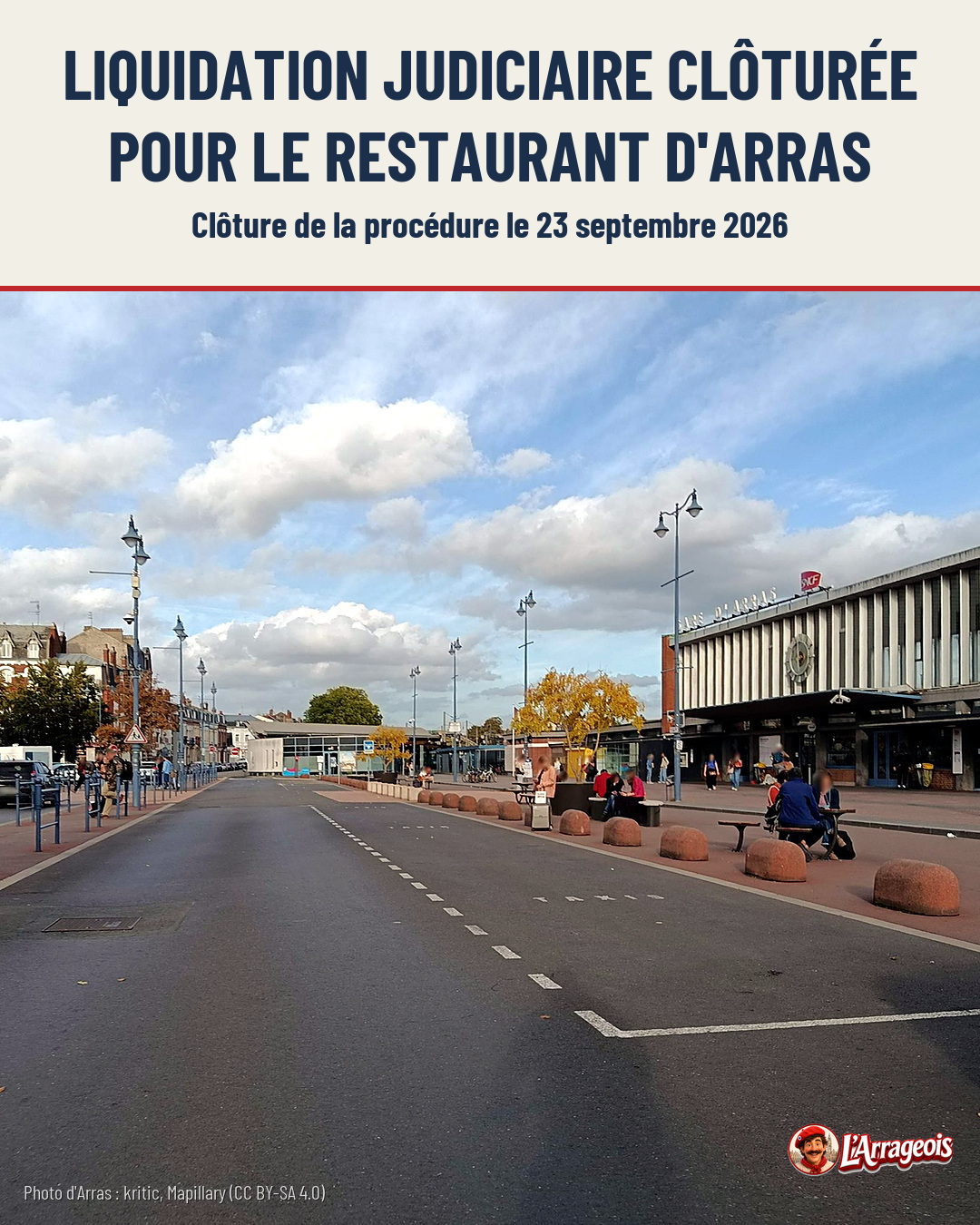 Une rue pavée d'Arras avec des lampadaires, des bollards en pierre, des personnes assises sur des bancs et un bâtiment commercial au loin.