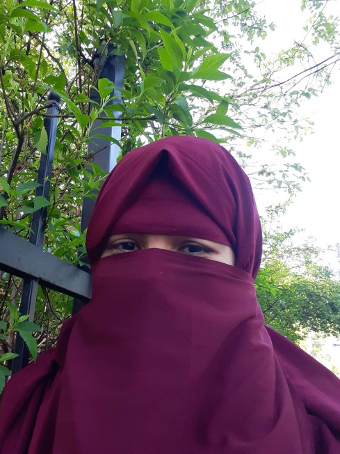Woman wearing pink veil (niqab and jilbab) over hair and face, black eyes with no makeup visible
