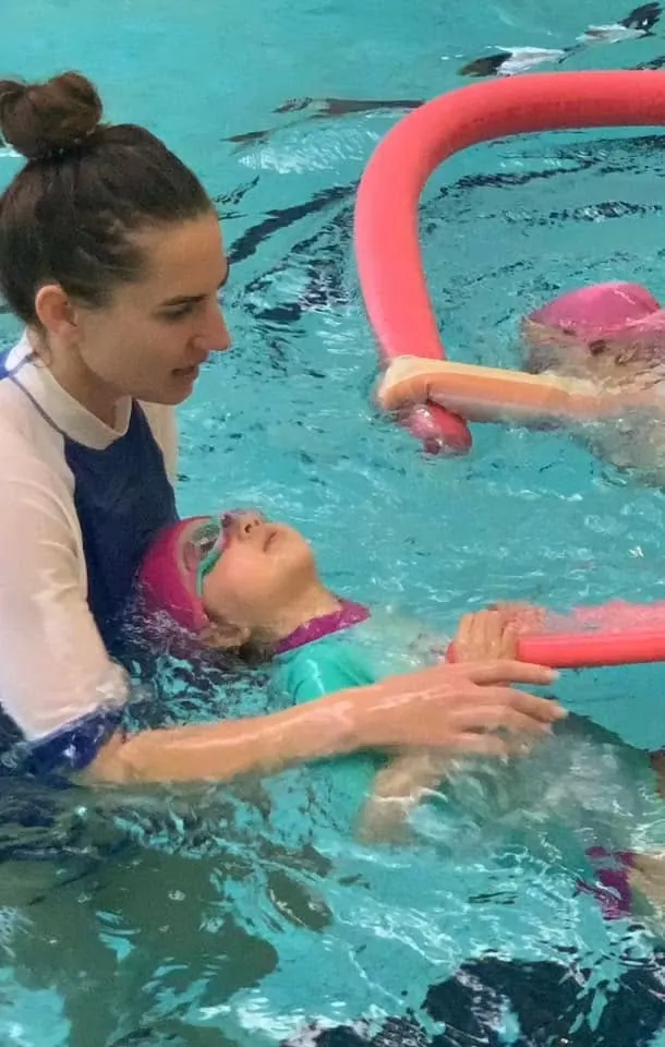 A Pod Squad instructor calmly supporting a child floating on their back