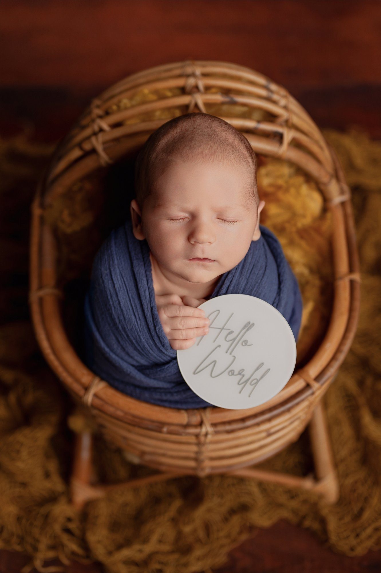 Peaceful newborn baby in navy blue wrap cradled in a woven basket during professional newborn photography session