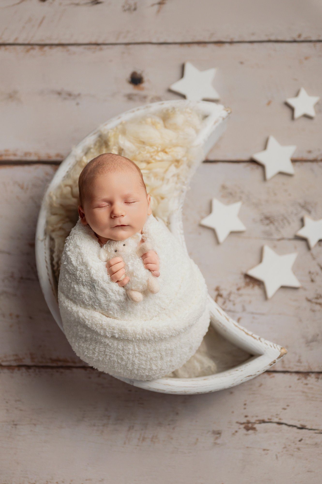 Sleeping newborn baby in blue wrap holding small teddy bear, artistic newborn portrait photography