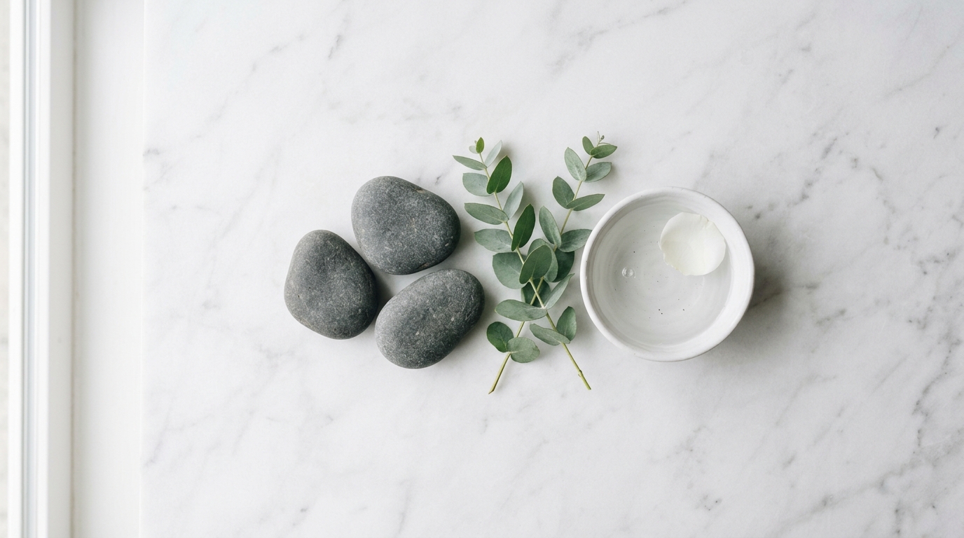 Lymphatic Drainage Massage — Complete Guide Spa wellness flat lay with smooth grey river stones, eucalyptus sprigs and white ceramic bowl on white marble
