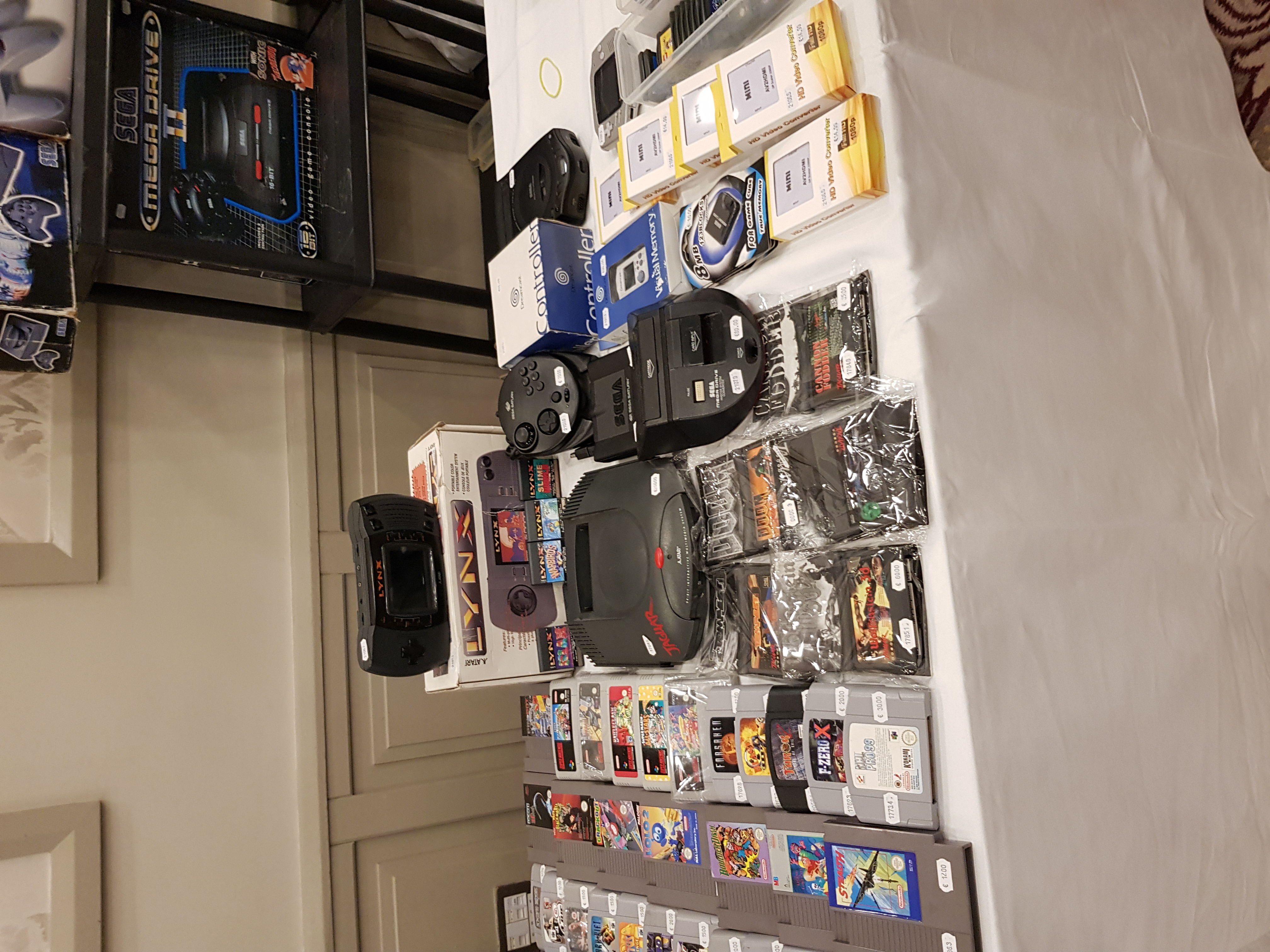 Some retro games, consoles, and accessories laid out on a table, including NES, SNES, N64, Atari Lynx and Jaguar, Sega Mega Drive, Saturn, and Dreamcast.