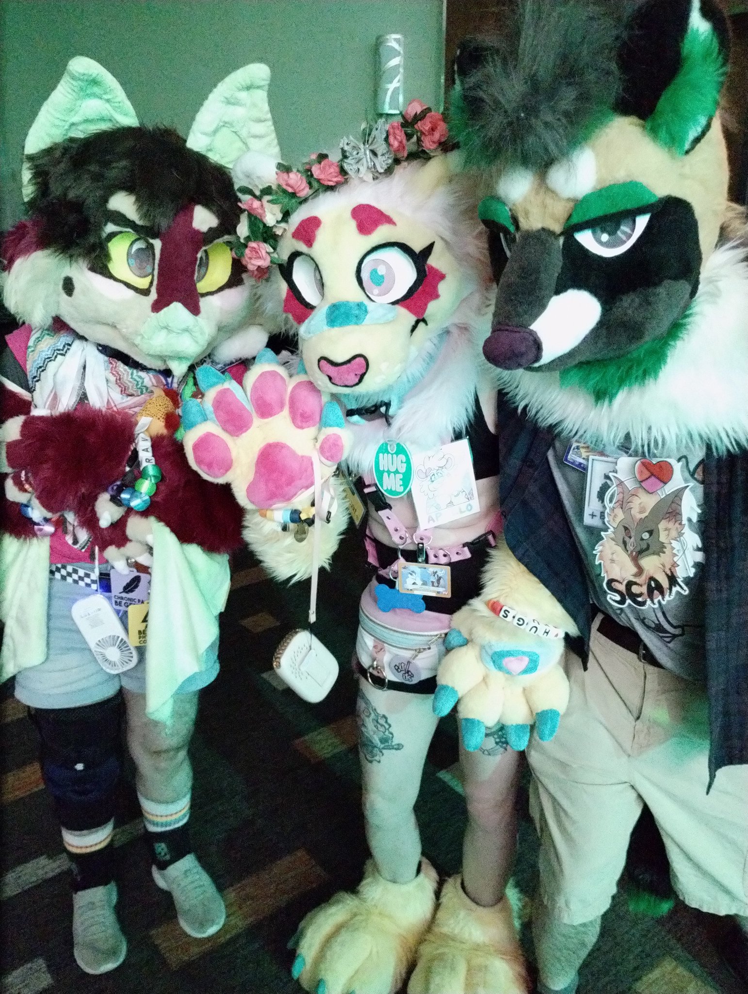 A group of fursuiters; a multicoloured bat, a multicoloured lion, and a brown, tan, white and green civet