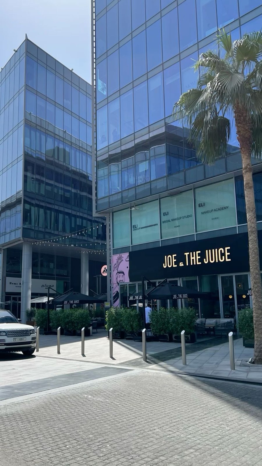 A sunlit city plaza with a blue-glass tower, a black storefront and a tall palm, the kind of real location photograph that works as an environment reference