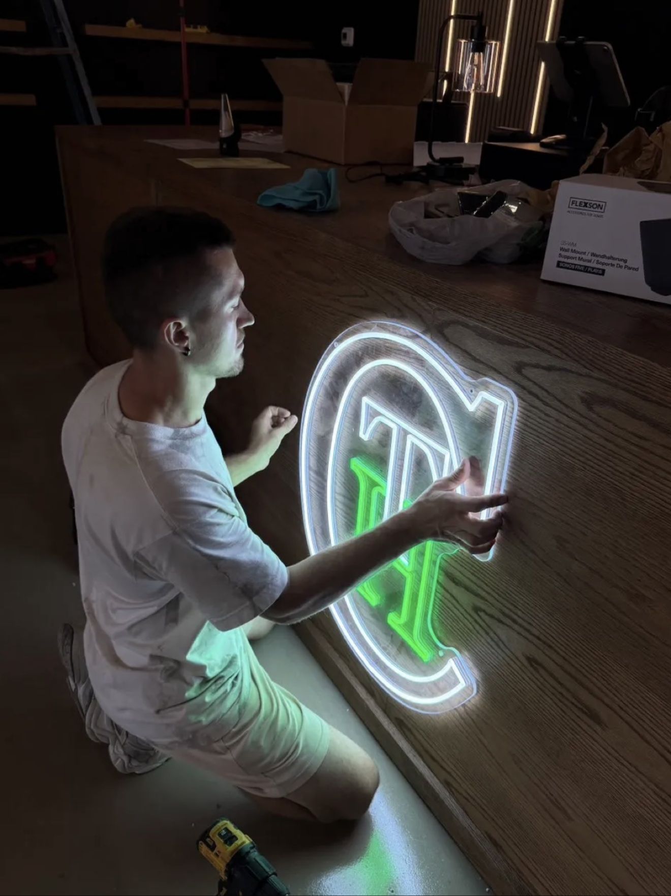 Aleh fitting a glowing neon sign onto a wooden counter