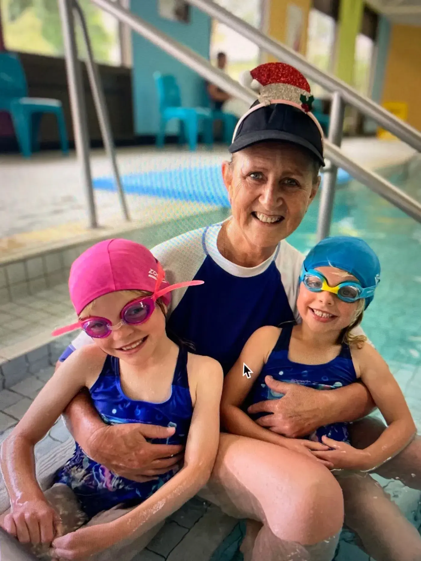 Two young Pod Squad swimmers smiling at the pool edge with their instructor