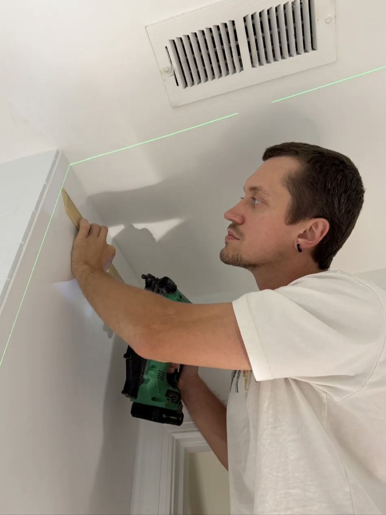 Aleh fitting trim with a nail gun, following a laser level line